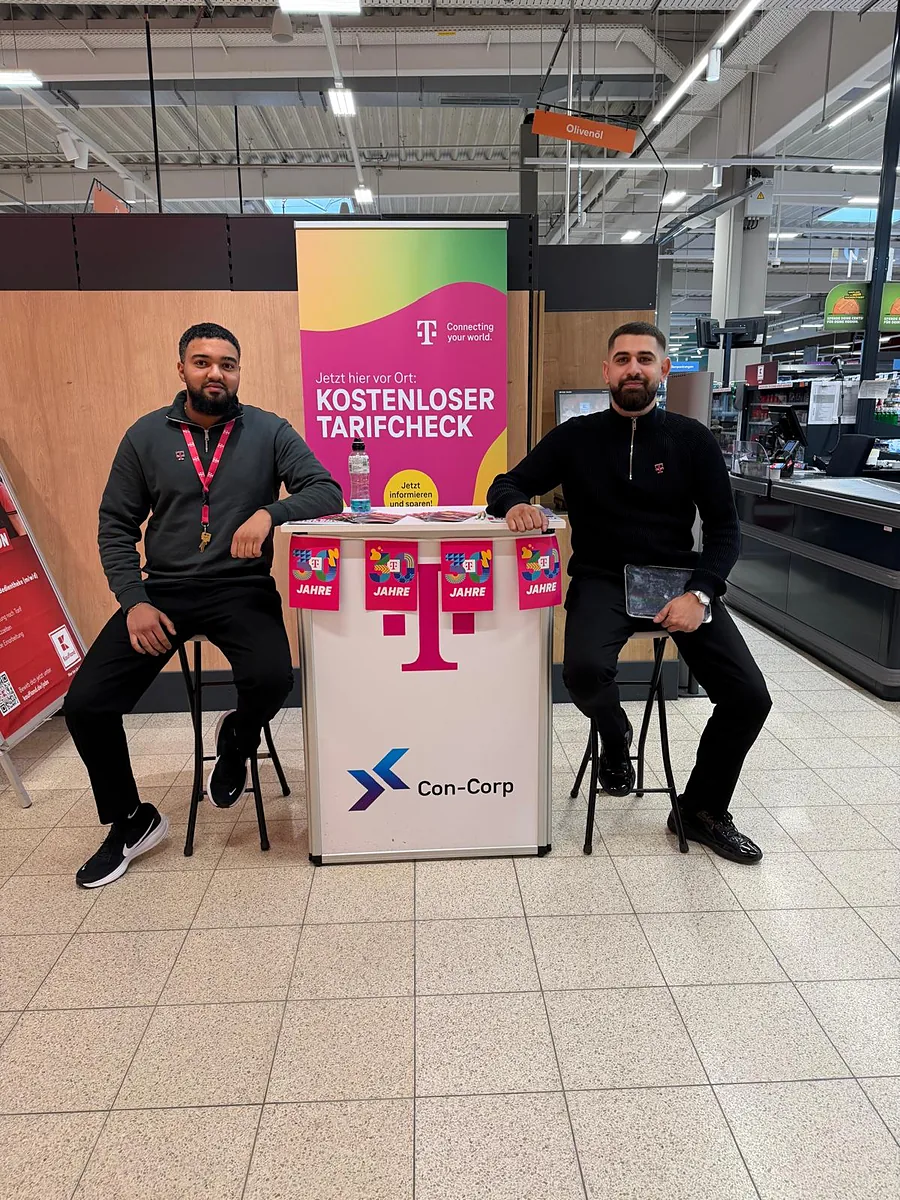 Zwei Promoter sitzen an unserem Stand mit Telekom und Con-Corp Logo im Supermarkt